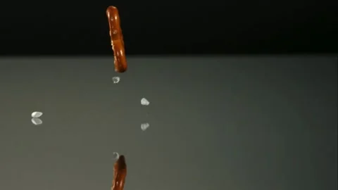 Salty pretzels falling and bouncing on a dark reflective surface Stock Footage 327788795