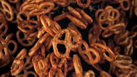 Salty pretzels fly and fall on a black background. Filmed on a high-speed camera Stock Footage 322807704