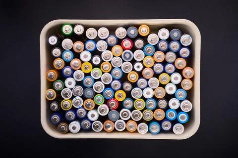 Samall AA batteries in a plastic box on a black table, ready to be recycled. Stock Photos