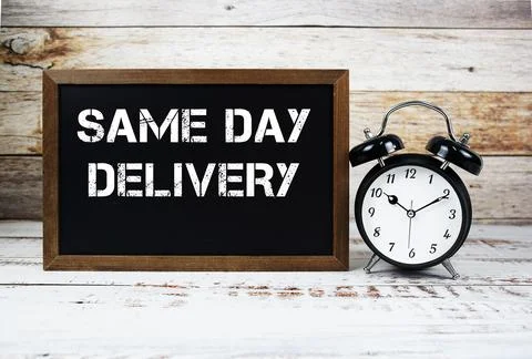 Same Day Delivery text message and alarm clock on wooden background Stock Photos