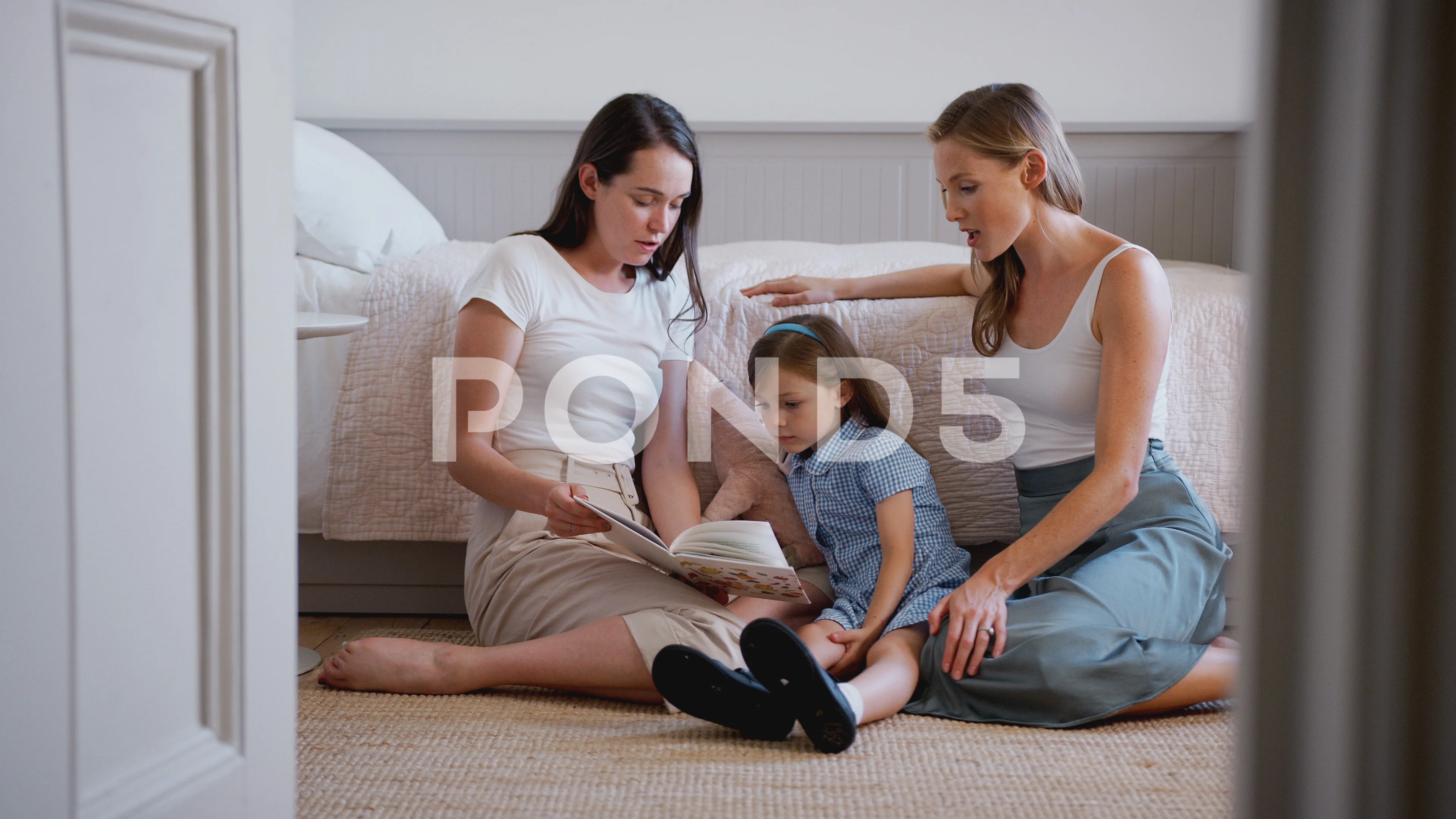 Same Sex Female Couple Sitting On Bedroom Floor Reading Book With Daughter  At