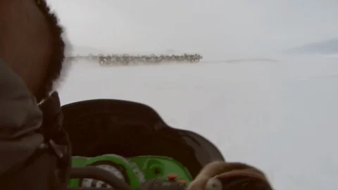 Sami sitting on a moving skidoo while herding the reindeer over a hill Video stock 107308284