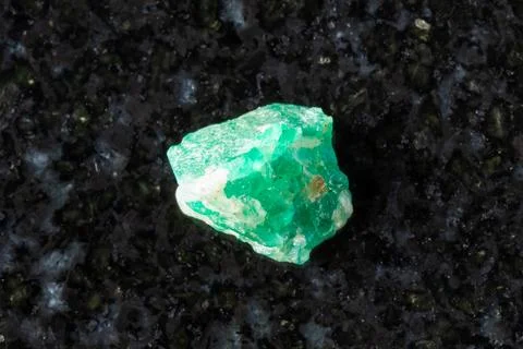 Sample of raw emerald mineral on black granite Stock Photos