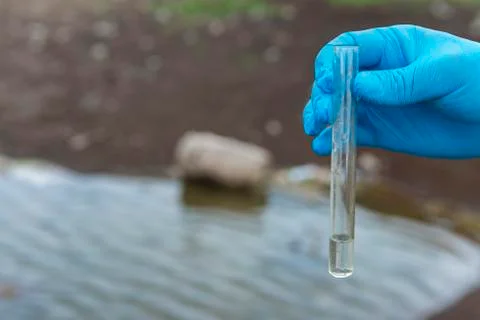 Sample water from the river for analysis. Hand in glove holding a test tube.e Stock Photos