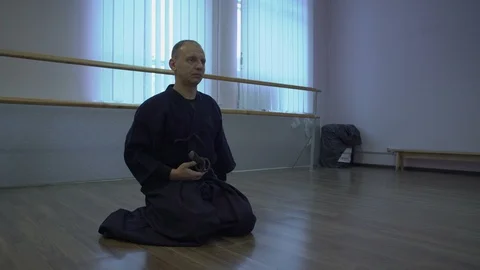 The Samurai Sits on the Floor and Binds Katana's Sword to the Belt, Then Rises Stock Footage 85917969