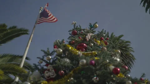 San Francisco, CA - Dec 12, 2024: Low angle of decorated pine tree and US flag Stock Footage 333615567