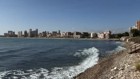 San Juan beachfront in Spain with clear waters, urban skyline, and rocky shore Stock Footage 294387253