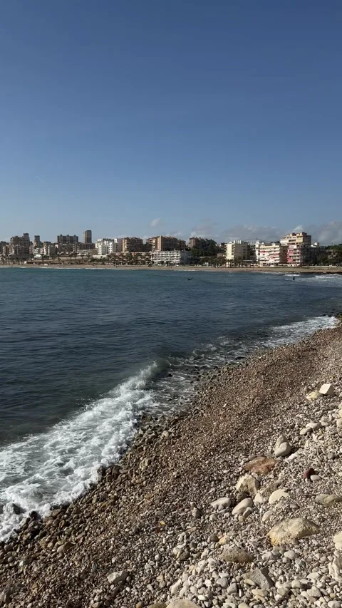 San Juan beachfront in Spain with clear waters, urban skyline, and rocky shore Stock Footage 294387258
