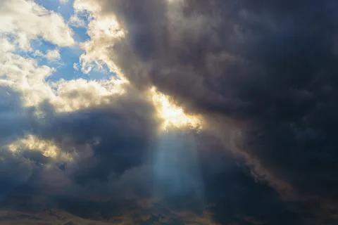 San ray breaks through the gap in a large dark cloud covering the blue sky. Stock Photos