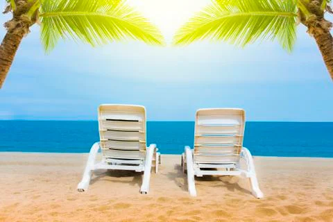 Sand beach with coconut trees with two chairs and bokeh beach tropical backgr Stock Photos