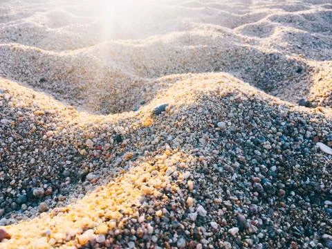 Sand beach texture background with rays of the sun. Detail of the grains of c Stock Photos