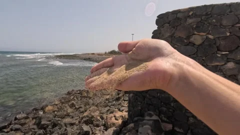 Sand being blown from a hand on a windy day overlooking a beach Stock Footage 289280993