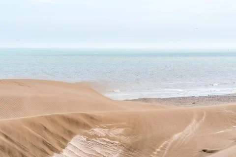Sand blown from a large dune by the wind with the horizon in the sea behind it. Stock Photos