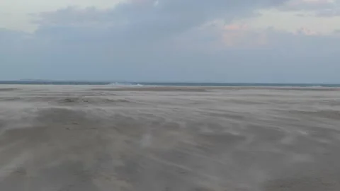 Sand is blown over an endless beach. Slow-motion of sand blown by the wind. Video stock 220521030