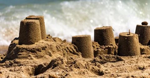 Sand castle in the foreground against the background of a wave of the sea Stock Photos