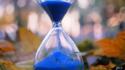 Sand clock with blue sand. Ten minute sand clock on autumn street background Stock Footage 118771367