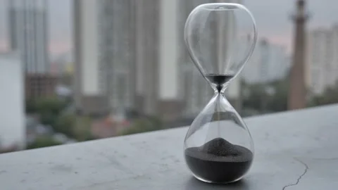 Sand clock measuring time with grey sky in evening time over city blurred Video stock 173709278
