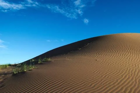 Sand dune beneath a deep blue sky Stock Photos