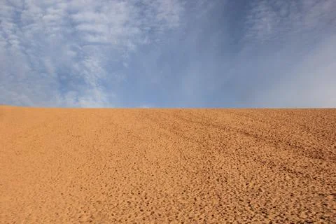 Sand dunes with cloudy blue sky behind it Stock Photos