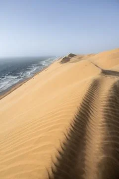 Sand dunes with wave patterns and sea in evening light, wind blowing sand across Stock Photos