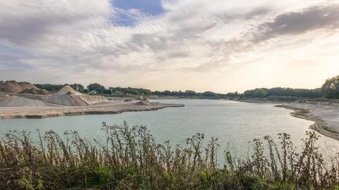 Sand extraction site with a large lake and piles of sand under a cloudy sky Stock Photos