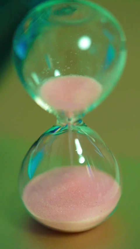 Sand flowing inside hourglass standing on surface. Pink grains running Stock Footage 325431590