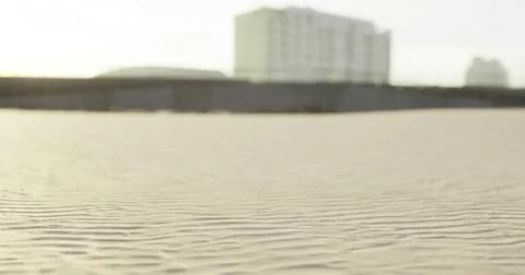 Sand formations stretch across the beach near a modern building at sunset Ilustración de archivo