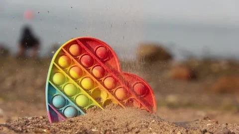 Sand pouring on a trend rainbow bubble toy - Pop it. Beach and sea background. T Stock Footage 156983148