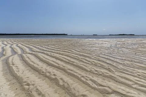 Sand shore with wave pattern ripples lines with water on a sunny day Stock Photos