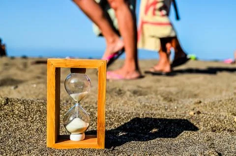 A sand timer is on the beach with a person walking behind it Stock Photos