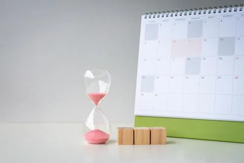 Sand timer with three blank wooden toy blocks next to a calendar. Foto stock