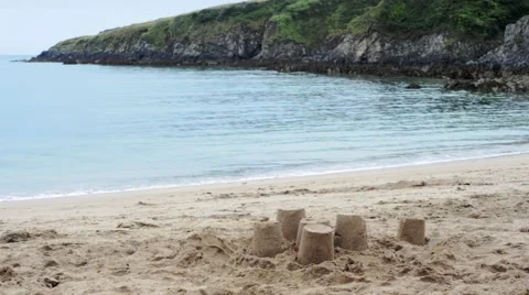 Sandcastles on the beach, gentle waves lapping in a rugged rocky cove Stock Footage 65458136