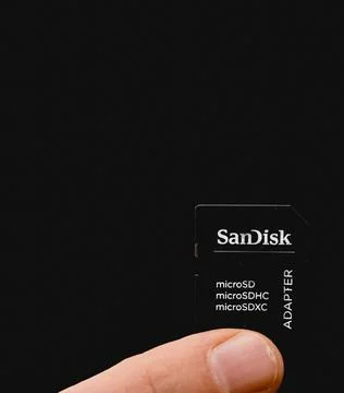 Sandisk memory card adaptor held between two fingers. Close up. Stock Photos