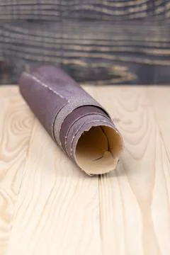 Sandpaper twisted into a roll lies on a wooden board. Close-up. There is a ti Stock Photos