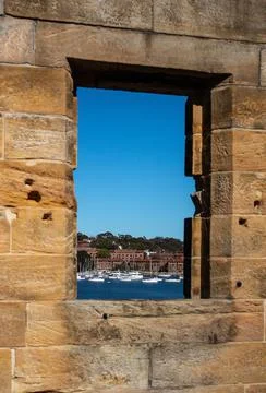 Sandstone brick wall with open window showing boats on water against blue sky Stock Photos