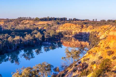 Sandstone eroding cliffs over houseboat moored in Murray River at sunset. Riv Foto stock