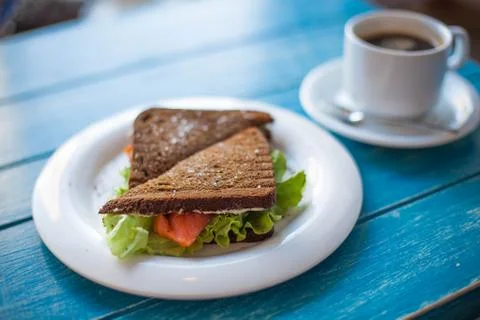 Sandwich of rye bread with red fish and lettuce and a cup of coffee. Stock Photos