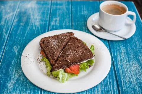 Sandwich of rye bread with red fish and lettuce and a cup of coffee. Stock Photos