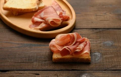 Sandwich with a white square slice of bread and slices of prosciutto on a w.. Stock Photos