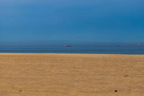 Sandy beach and distant cargo ships on Baltic Sea shore at midday Stock Photos