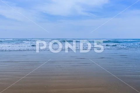 Sandy beach and rough ocean waves and white caps under a blue sky with low wi Stock Photos