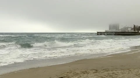 Sandy beach and rough sea,pier and high-rise hotel building in fog,dense clouds Stock Footage 65187200
