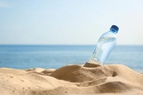 Sandy beach with bottle of refreshing drink on hot summer day, space for text Stock-Fotos