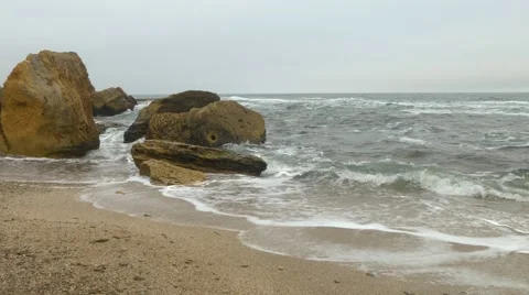 Sandy beach with choppy rough sea, yellow rocks, dense gray clouds covering sky. Stock Footage 65201566