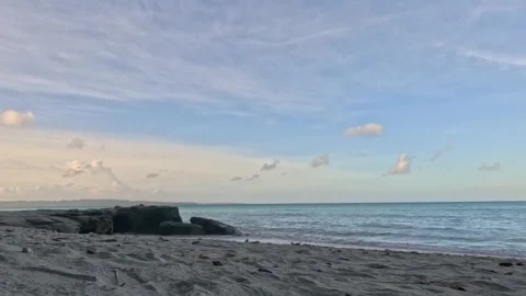 Sandy Beach with Gentle Ocean Waves and Distant Rock Formations Under Blue Sky Stock Footage 340413899