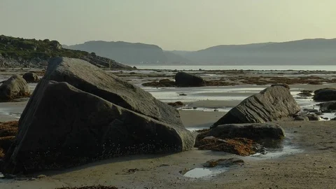 Sandy beach with huge rocks and clumps of seaweed at low tide. Stock Footage 74379334