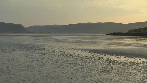 Sandy beach at low tide against low mountains and a village in the distance. Stock Footage 74481848
