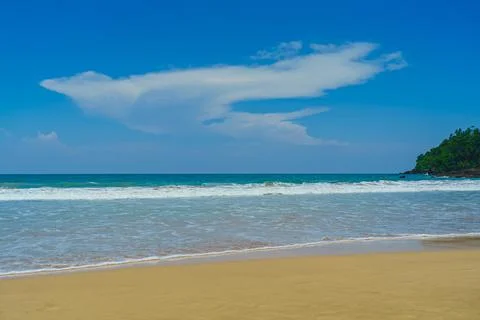 Sandy beach with low waves and clouds in the blue sky Stock Photos