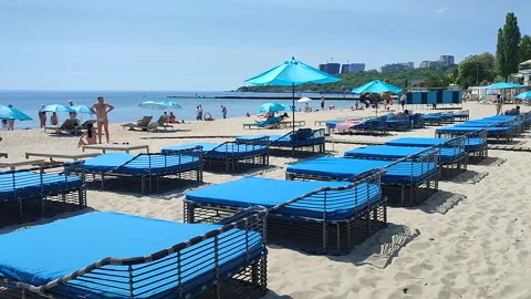 Sandy beach near sea with empty blue sun loungers on sunny hot summer day Stock Footage 327669506