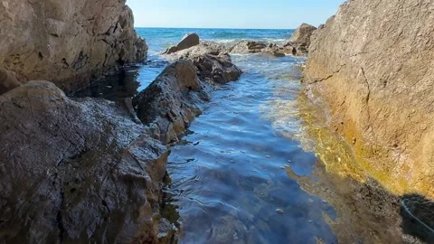 Sandy beach nestled between rocks with clear water reflecting sunlight on a Stock Footage 339067129